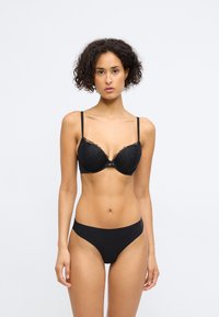Sutiã preto de renda com copos almofadados e alças ajustáveis, apresentando um design floral. Combinado com roupa interior preta sem costuras correspondente.