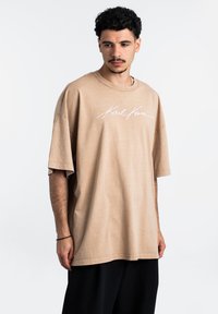 Ruda per didelį t-shirt, pagamintas iš minkštos medvilnės, su baltu logotipu ant krūtinės. Siluetas laisvas, su trumpomis rankovėmis ir apvaliu iškirpimu.