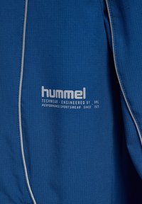Blauer Sportstoff mit weißem „hummel“-Logo und Schriftzug „Techwear Engineered by HML Performance Sportswear Since 1923.“