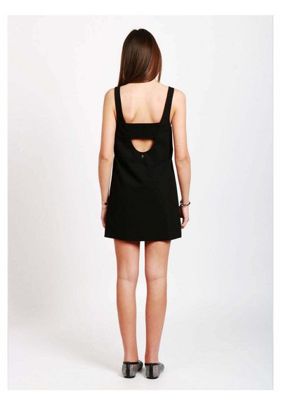 Vestito nero senza maniche con dettaglio sulla schiena scoperta, silhouette a trapezio e tessuto morbido; abbinato a scarpe nere piatte con texture.