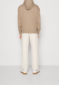 Sudadera beige con capucha, con un corte holgado y dobladillo acanalado, combinada con pantalones anchos color casi blanco y zapatillas blancas con suela marrón claro.