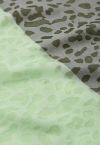 Gros plan sur un tissu présentant des motifs d'animaux vert clair et gris, avec une texture lisse et légèrement froissée.