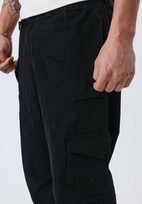 Pantalones cargo negros con múltiples bolsillos. Fabricados con un tejido duradero, cuentan con un corte relajado y una cintura elástica. Textura suave.