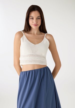 Top corto bianco in maglia con scollo a V e motivo traforato, abbinato a una gonna azzurra fluente. Caratteristiche principali includono spalline regolabili.