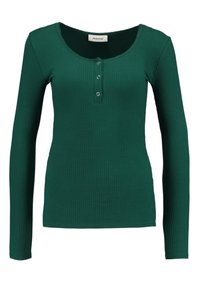 Haut à manches longues en ribbed de couleur vert foncé, avec un col rond et une patte de boutonnage à trois boutons sur la poitrine. Texture douce avec une coupe ajustée.