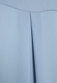 Tissu bleu clair avec une texture lisse présentant un détail de pli. Le matériau semble doux et tombe doucement. Aucun motif ni accessoire visible.