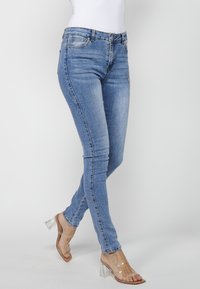Skinny blue jeans in light denim with a mid-rise waist, featuring distressed detailing and a smooth, slightly stretchy texture.