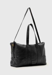 Black leather duffel bag with dual top handles and a removable shoulder strap. Features a gold zipper and visible stitching details.