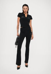 Haut noir ajusté à manches courtes et pantalon évasé, tous deux avec un logo discret. Tenue accompagnée d'un petit sac à main noir et de talons aiguilles.