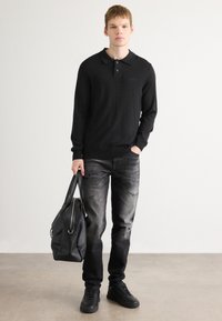 Polo din tricot negru cu guler, asortat cu blugi gri închis, uzati, și adidași negri. Modelul ține o geantă din piele neagră.