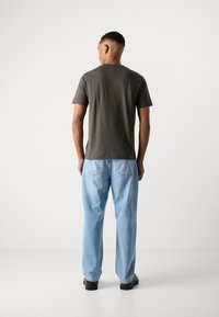 Dark green short-sleeve t-shirt paired with light blue loose-fit jeans. The jeans have a faded texture and visible stitching on the pockets.