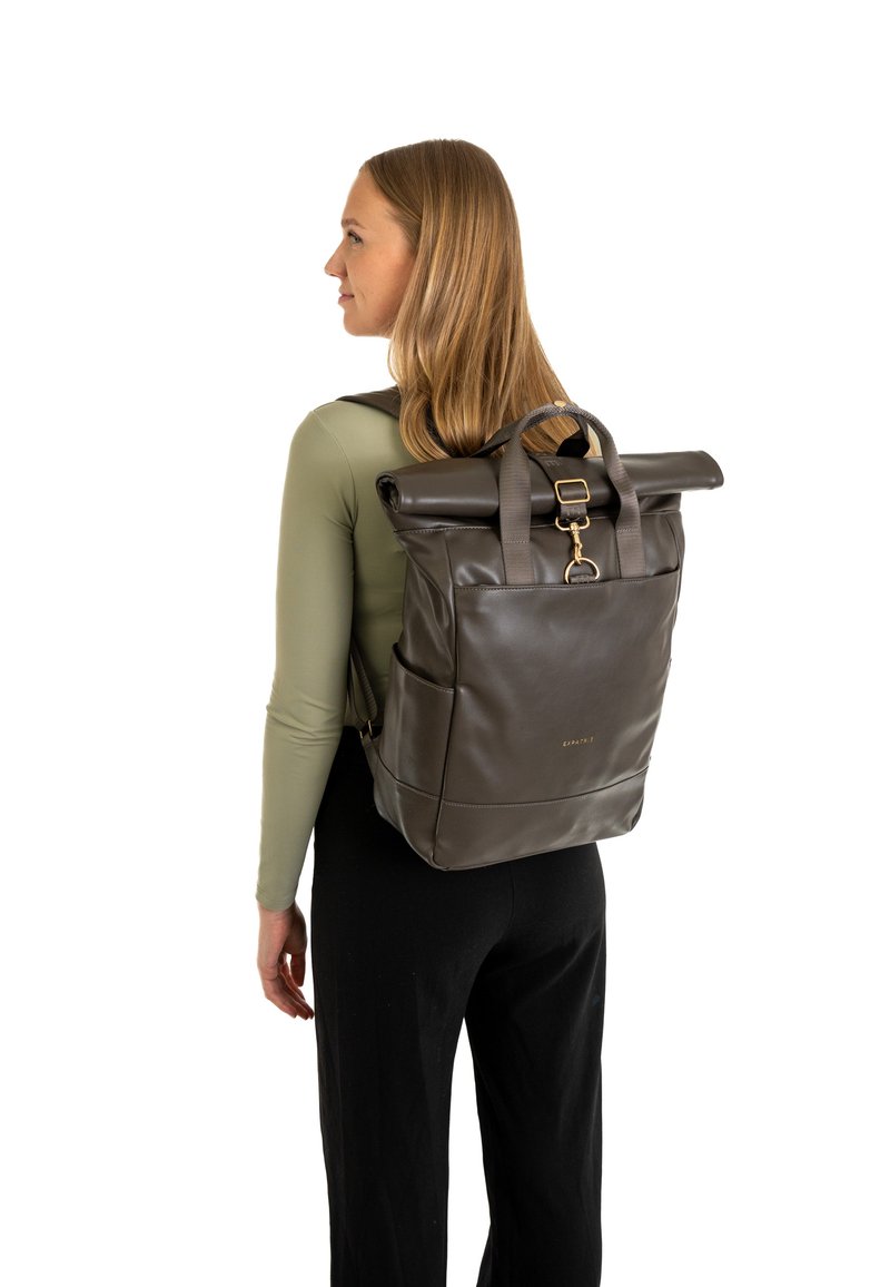 Zaino roll-top in pelle marrone scuro con chiusura in metallo dorato e manici superiori. Presenta un design minimalista con tasche laterali.