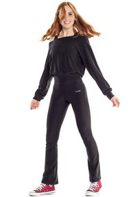 Black long-sleeve top with off-shoulder design, paired with black fitted pants. Model wears red Converse shoes, showcasing a relaxed outfit.