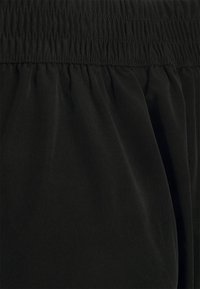 Czarna elastyczna talia z marszczoną fakturą, wykonana z miękkiego, gładkiego materiału, który swobodnie opada, tworząc luźne dopasowanie.