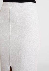 Šedá pletená sukně s vysokým pasem, bočním rozparkem a hladkým povrchem. Švy zvýrazňují tvarující design.
