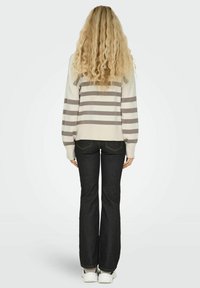 Pull à rayures claires avec des manches longues, associé à un jean évasé foncé. Les chaussures sont des baskets blanches. Vue de dos.
