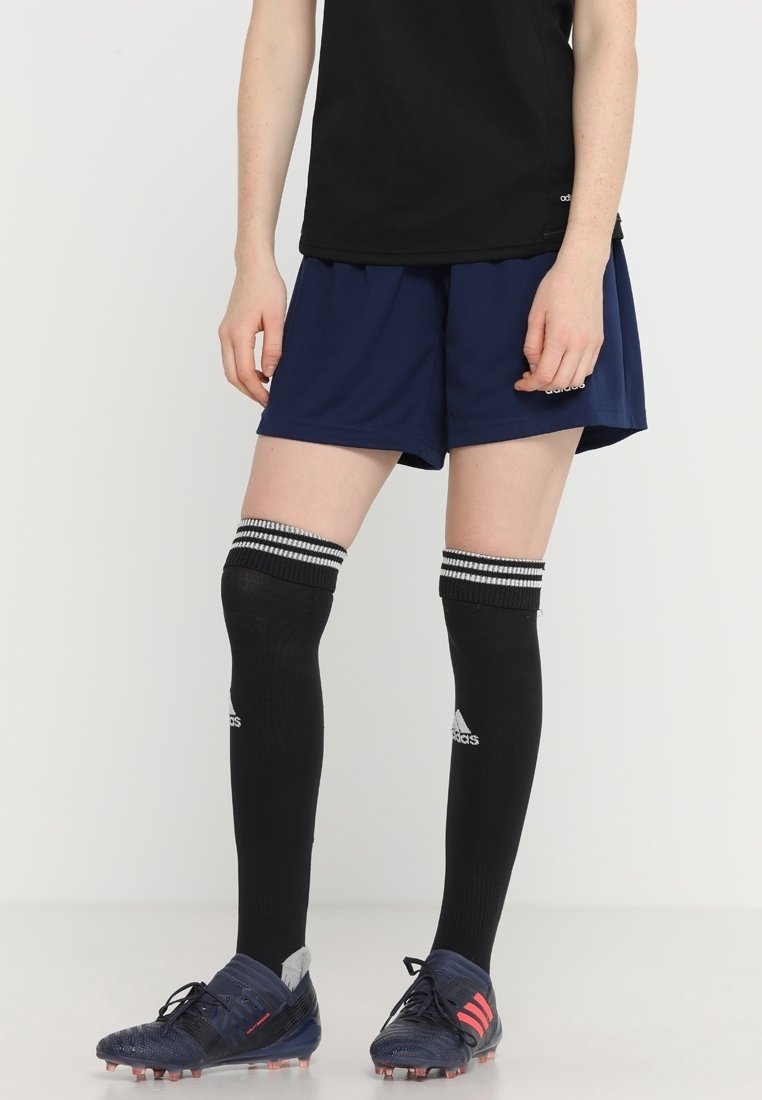 Camiseta deportiva negra, pantalones cortos azul marino, calcetas negras hasta la rodilla con rayas blancas y botas de fútbol azules con acentos rojos.