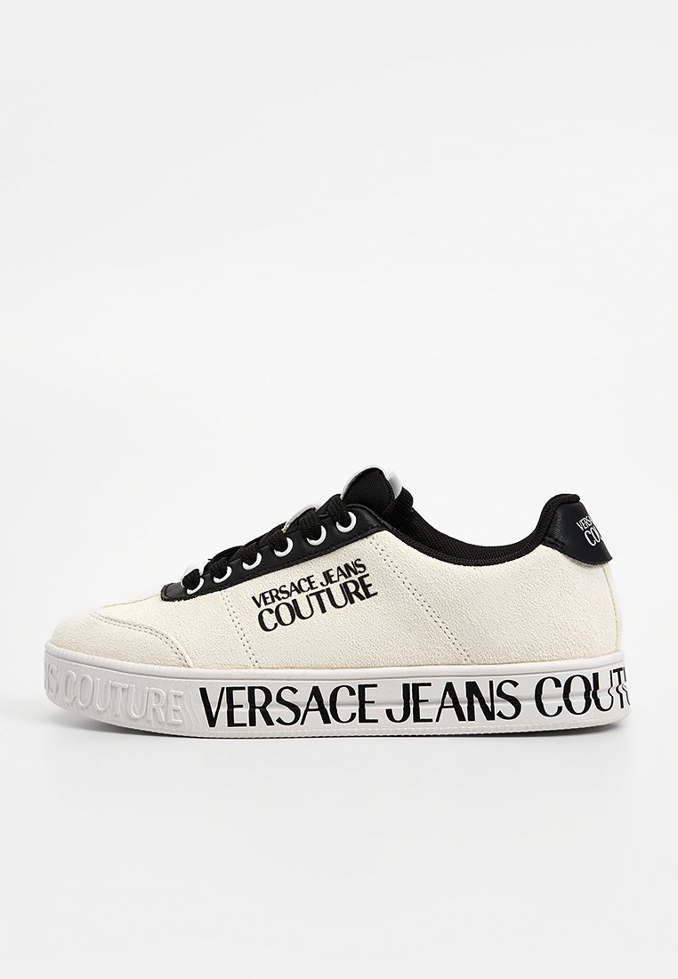 Zapatillas de lona blanca con detalles en negro, cordones negros y estampado de logo en el lateral y la suela, diseño de punta redonda.