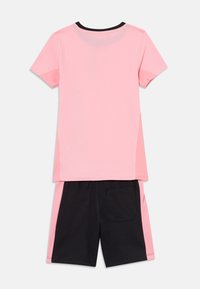 Lyserød T-shirt med korte ærmer og sort halsudskæring, parret med sorte shorts med en sidelomme og lyserød aksent på siderne.