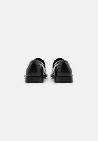 Chaussures en cuir noir avec une finition polie, bout arrondi et un talon bas. Présentent des coutures le long des coutures et un design à l'arrière ouvert.