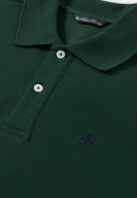 Tmavě zelené polo tričko vyrobené z texturované látky. Obsahuje límeček, tři bílé knoflíky a na hrudi vyšívané logo v námořnické modři.