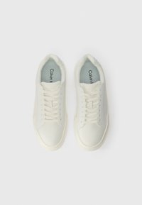 Bílé tenisky s hladkým koženým svrškem, zaoblenou špičkou a plochými tkaničkami. Obsahují jemné logo na jazyku a polstrovanou podšívku.