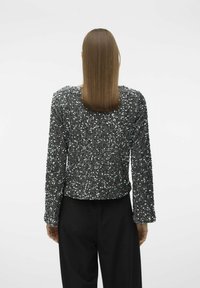 Top negro de lentejuelas de manga larga con cuello redondo, con una superficie texturizada y un corte ajustado, combinado con pantalones negros.