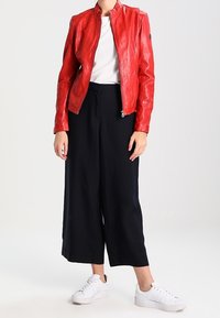 Czerwona, skórzana kurtka motocyklowa z zamkiem z przodu, połączona z granatowymi spodniami o szerokich nogawkach i białymi tenisówkami. Gładka faktura, dopasowany krój.