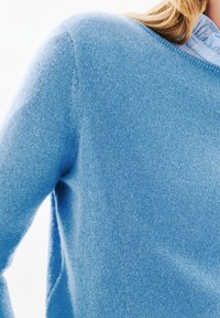 Jasnoniebieski sweter wykonany z miękkiej, dzianinowej tkaniny. Posiada okrągły dekolt oraz dopasowany krój, eksponując gładką teksturę.