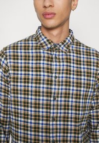 Camisa de botón con un patrón a cuadros en azul, naranja, blanco y verde. Presenta un cuello y botones oscuros, confeccionada en una tela suave.