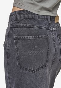 Svarta denimjeans med hög midja, framträdande bakfickor och diskret branding på höger ficka. Strukturerad tyg med sömdetaljer.