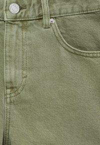 Gros plan sur la poche avant d'un jean en denim vert olive avec détails de bouton métallique et rivet.