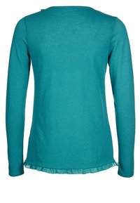 Långärmad topp i teal färg gjord av mjukt tyg med rund halsringning och volang nertill. Texturerat, lätt material.