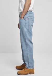 Lys blå denim jeans med avslappet passform, med frontlommer, en baklomme og brune snørebåndsstøvler. Jeansen har en glatt tekstur og minimalt med hardware.