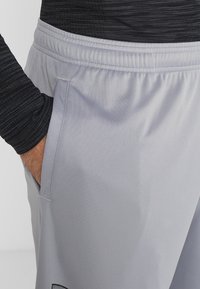Lichtgrijze sportbroek met een elastische tailleband en zijzak, gemaakt van een gladde, ademende stof. Minimalistisch ontwerp met zwart logo.