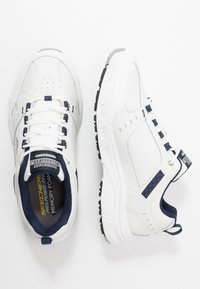 Scarpe da atletica bianche con dettagli blu navy, realizzate in materiali mesh e sintetici, punta perforata, soletta imbottita e suola esterna in gomma nera.