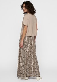 Beige cropped t-shirt met korte mouwen, gecombineerd met een lange, bruin schubbenpatroon rok. De outfit heeft een ontspannen silhouet en een zachte textuur.