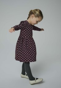 Körsbärsröd A-linjeformad klänning med blommönster, långa ärmar och en rynkad midja. Grå ribbade strumpbyxor och gräddvita ballerina med remmar ger kontrast.