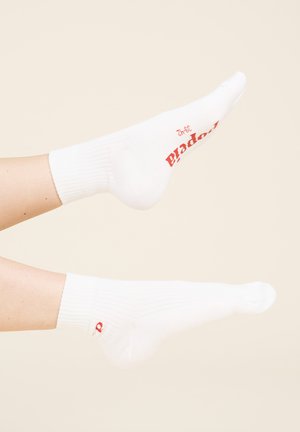 Weiße Knöchelsocken mit geripptem Bund; verfügen über rote Markenkennzeichnung auf der Oberseite und ein kleines rotes Logo an der Ferse. Glatte Stofftextur.