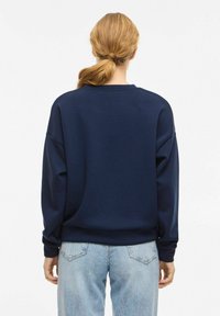 Sweat-shirt bleu marine à coupe décontractée, col rond et épaules tombantes. Tissu doux avec une texture subtile, associé à un jean bleu clair.