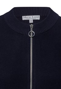 Marineblaue gerippte Strickjacke mit hohem Kragen, ausgestattet mit einem silbernen Reißverschluss und einem runden Reißverschlussanhänger, beschriftet mit "Marie Lund, Kopenhagen, Größe S".