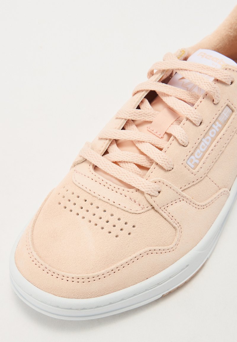 Zapatilla de ante rosa claro con detalles perforados, cordones planos y una suela de goma blanca. Logotipo de Reebok en el lateral.