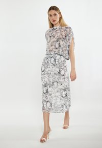 Doorzichtig wit blouse en bijpassende rok met zwarte bloemmotieven. Heeft korte mouwen en een hoge halslijn. Open-teen hakken.