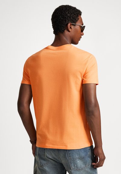 Πορτοκαλί βαμβακερό μπλουζάκι με κοντά μανίκια, στρογγυλή λαιμόκοψη, λεία υφή και χαλαρή εφαρμογή, εμφανιζόμενο από πίσω.