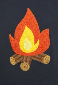 Broderad märkning med eld i orange och gula nyanser, med texturerade lågor ovanför bruna stockar på en mörk bakgrund.