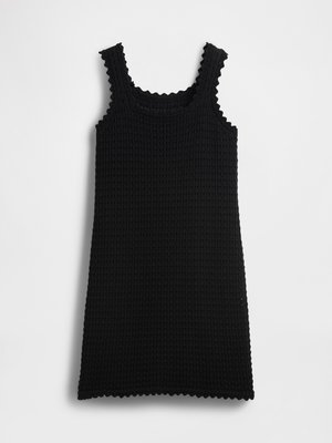 Vestido preto sem mangas com malha texturizada em waffle e bordas em forma de concha nas alças, decote e barra, disposto em plano sobre um fundo branco.
