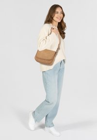 Hellbraune Wildleder-Crossbody-Tasche mit Klappenverschluss und verstellbarem Riemen. Getragen mit einem cremfarbenen Pullover und hellblauen Jeans in lockerer Passform.