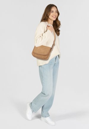 Borsa a tracolla in suede tan con chiusura a pattina e tracolla regolabile. Indossata con un maglione color crema e jeans azzurri chiari, con una vestibilità rilassata.