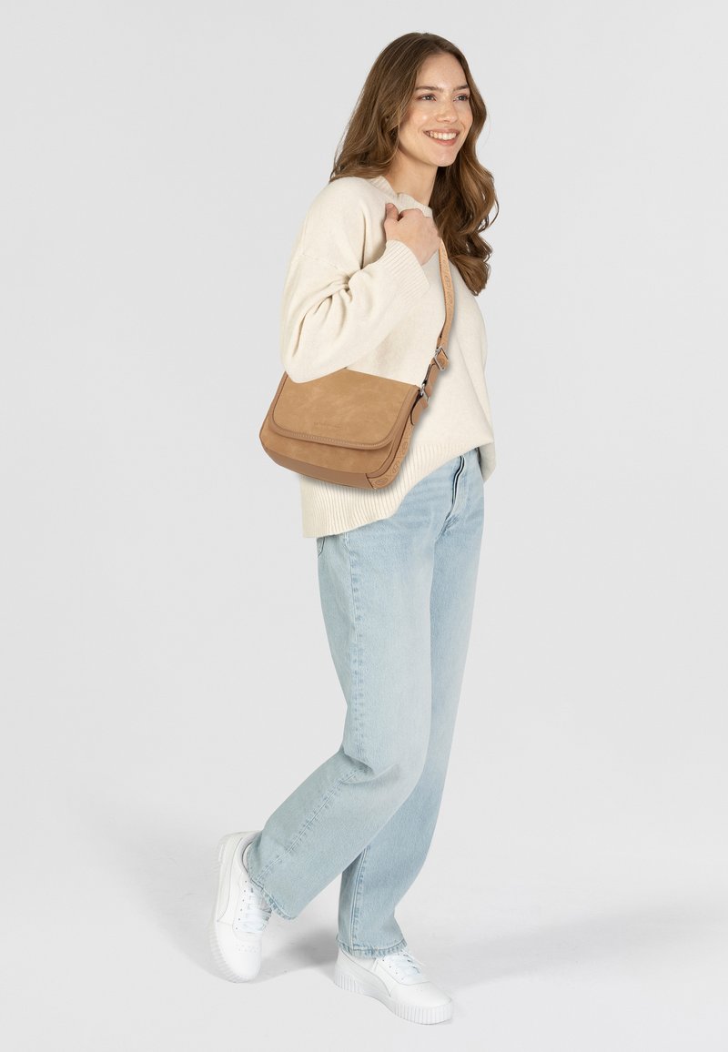 Hellbraune Wildleder-Crossbody-Tasche mit Klappenverschluss und verstellbarem Riemen. Getragen mit einem cremfarbenen Pullover und hellblauen Jeans in lockerer Passform.