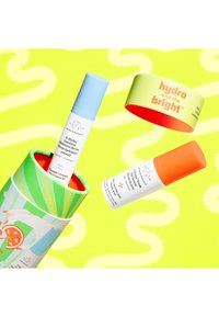 Three skincare products from Drunk Elephant: a blue capped serum, a white bottle with orange cap, and a colorful cylindrical packaging. Bright, playful colors.